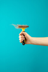 A hand holds a furminator with combed fur on a plain turquoise background. Grooming salon. Care for shedding pets, cats or dogs. Concept of seasonal pet molting, dog and cat care at home.