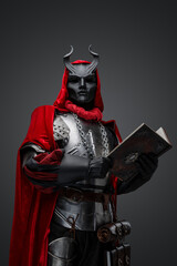 Studio shot of creepy dark cultist dressed in red robe holding book.