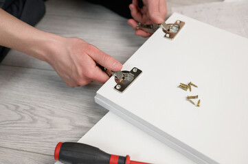 Assembling furniture. A worker inserts a hinge into a wooden closet door. Adjustment of fittings,...