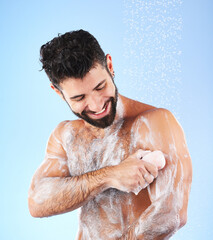 Obraz na płótnie Canvas Soap, shower and man with water splash, smile and hygiene in studio for wellness, cleaning and grooming. Skincare, healthy skin and happy male with foam, cosmetics and washing body on blue background