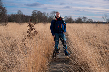 Man with dog walking wooden plank path through a peat bog