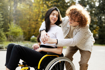 Positive, smiling man in glasses with curly hair hugs a girl on the street. A disabled girl sits in a wheelchair.
