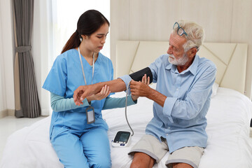 Happy caregiver checking blood pressure monitor and heart rate senior elderly man patient on bed at...