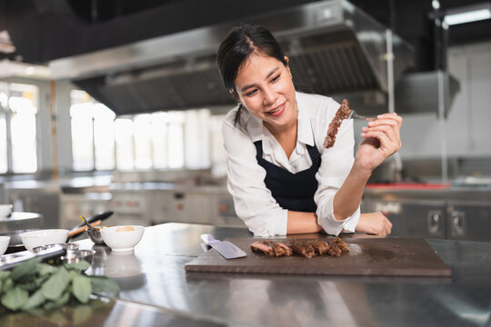 Happy student Asia woman chef with steak at kitchen background	
