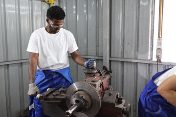 Multiethnic technicain mechanic or worker man in protective uniform using metal lathe machine operate polishing car disc brake at garage. Maintenance automotive and inspecting vehicle part concept