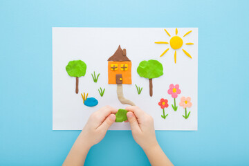 Baby boy hands making home yard with different colorful shapes from modeling clay on white paper....