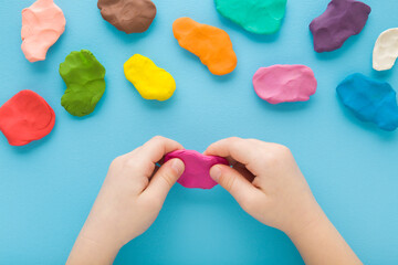 Baby boy hands holding and kneading modeling clay on light blue table background. Pastel color. Closeup. Top down view. Toddler development. Preparing material for making different colorful shapes. - Powered by Adobe