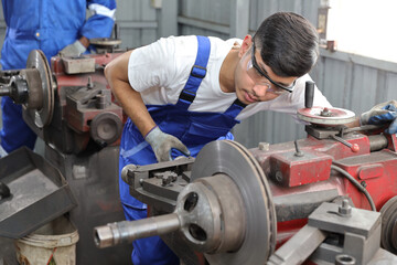 Multiethnic technicain mechanic or worker man in protective uniform using metal lathe machine operate polishing car disc brake at garage. Maintenance automotive and inspecting vehicle part concept