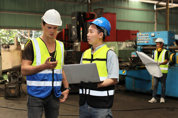 Technician engineer or worker man in protective suit standing and using walkie talkie radio while controlling or maintenance operation work lathe metal machine at heavy industry manufacturing factory