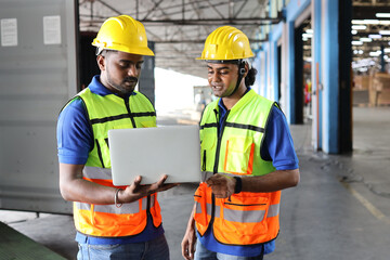 Group of warehouse workers with hardhats and reflective jackets using computer, walkie talkie radio and cardboard controlling stock and inventory in retail warehouse logistics, distribution center