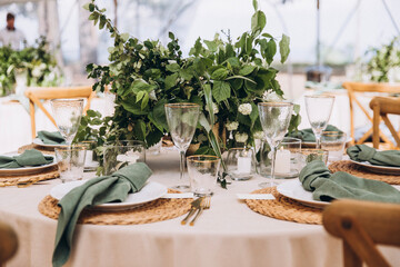 Wedding. Banquet. On the festive table with a tablecloth is a composition of flowers and greenery,...