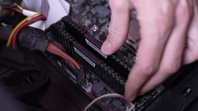 Close-up high-angle view of unrecognizable computer technician installing RAM memory into motherboard. Concept of desktop PC maintenance and service. Shooting in slow motion.