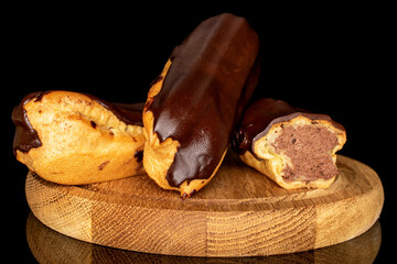 Two whole and one half chocolate eclairs on a wooden tray, macro, isolated on black background.