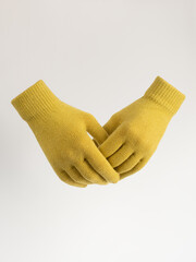 Gloves on an invisible mannequin. Yellow gloves on a light gray background studio shot. Women's knitted gloves, isolated.