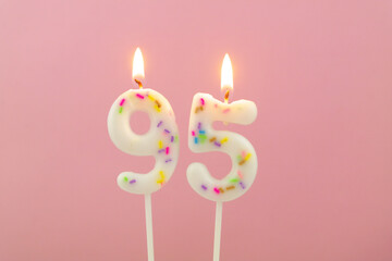 Burning white birthday candles on pink background, number 95