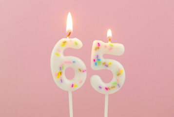 Burning white birthday candles on pink background, number 65