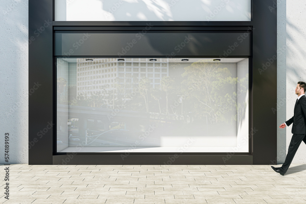 Poster businessman walking through sunlit empty showcase with light wall background behind window with spac