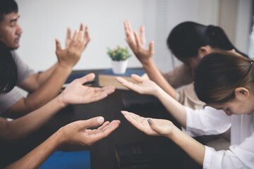 Group of religious people praying together indoors. group of people holding hands and praying while sitting in office.