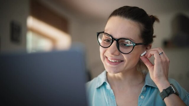 Portrait of a young adult caucasian woman wearing glasses taking a video call on a laptop.
