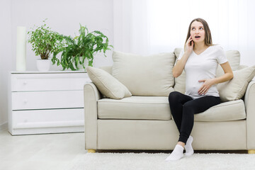 Obraz premium Photo of cute pregnant woman sitting on sofa.