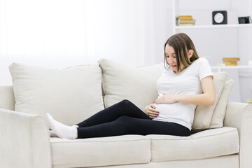 Pregnant woman put her hands on her stomach on white sofa.