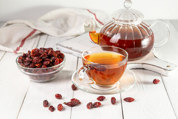 A cup of brewed rosehip medicinal plants herbal tea on a white wooden vintage table with dried rosehips