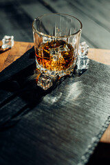 Glass of whiskey with ice cubes on black stone table. Side view with copy space alcohol concept.