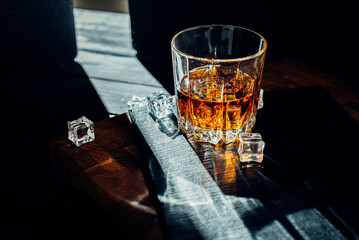 Glass of whiskey with ice cubes on black stone table. Side view with copy space alcohol concept.