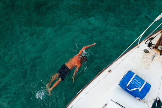 Man swimming next to sailboat through clear ocean, English Key, Belize