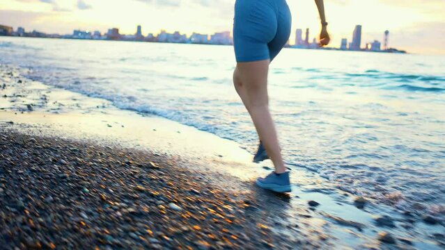 sports female running on the beach only the legs are visible, unrecognizable ,splashes of water and waves, view from the back