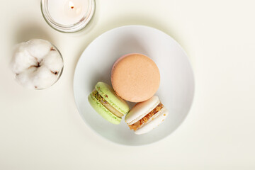 Beautiful composition of french colored assorted macarons on a white round plate from above on light beige background. An exquisite french dessert for a perfect breakfast.