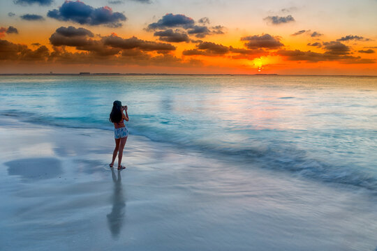 Woman photographing Caribbean Sea on beach at sunset, Isla Mujeres, Yucatan Peninsula, Mexico