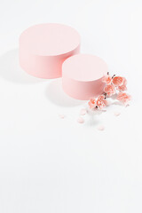 Two fashion spring cylinder podiums mockup with twig of gentle pink sakura flowers, petals in sunlight with shadow on white background for presentation cosmetic products, goods, vertical, top view.