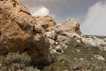 Big yellow weathered stone rock with lichen, cracks and dim green meadow in sunlight with fluffy...