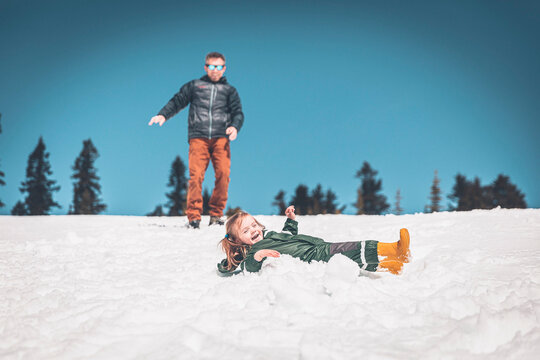 A small girl is sliding on here back with her father behind