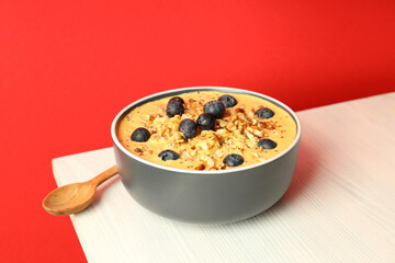 Smoothie with different ingredients on white wooden table against red background