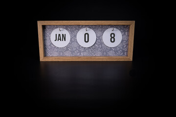 A wooden calendar block showing the date January 8th on a dark black background