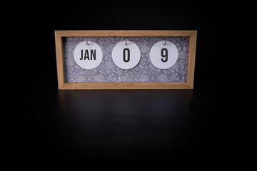 A wooden calendar block showing the date January 9th on a dark black background