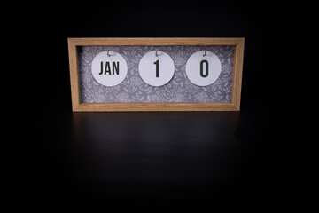 A wooden calendar block showing the date January 10th on a dark black background
