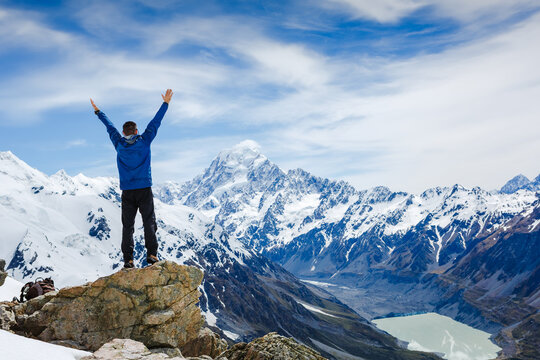 Hiker or traveller stands in winner pose at mountain top against mountains. Win or success concept
