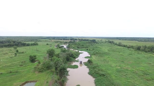 Drone camera video rotates to the right, with a view of a boat sailing over a river with meadows and trees on either side, in Indonesia's Way Kambas Forest National Park.