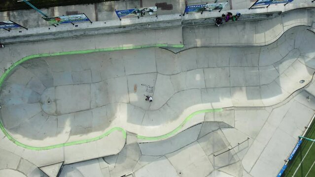 Topdown drone footage of a skateboarder in a skatepark pool. The skater falls down trying a trick. Drone flies upwards. Located at the "Converse skatepark" In San Borja district of Lima, Peru.