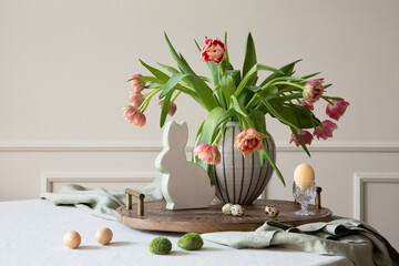 Interior design of easter dining room with colorful easter eggs, easter bunny sculptures, vase with tulips, wooden trace, beige wall with stucco, gray hen and personal accessories. Home decor Template