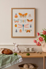 Warm composition of easter living room interior with mock up poster frame, wooden sideboard, vase with tulips, easter bunny, bread, beige cup, eggs and personal accessories. Home decor. Template