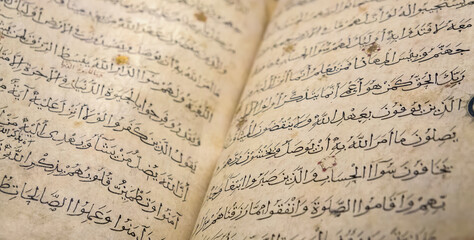 Ancient open book in arabic (verses of Quran or Koran Book Pages, Holy Islamic Text). Old arabic book manuscript pages. Selected focus, shallow depth. Ramadan, Islam or religion history concept - obrazy, fototapety, plakaty