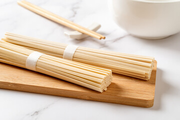 Dried udon nudles prepared for cooking. Raw asian vegan pasta from wheat flour on a bamboo cutting board, chopsticks and bowl over marble countertop. Japanese cuisine concept.