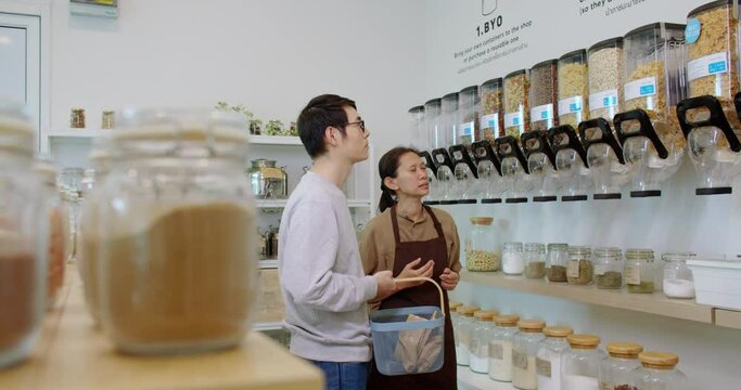 Female eco friendly store owner talking to client and advising customer bio organic goods product in plastic free zero waste grocery shop. Sustainable small local business SME startup go green market.