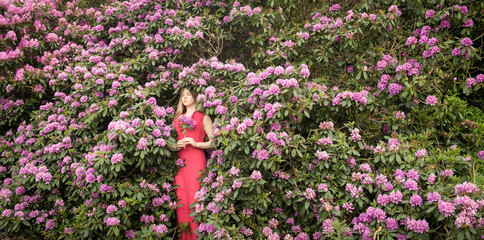 woman in pink dress standing in purple flower bush of rhododendron in park