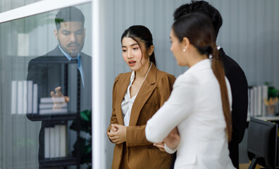 Millennial Asian professional businesswoman employee staff officer in formal business suit standing crossed arms with male female colleagues listening to Indian businessman discussing on glass board
