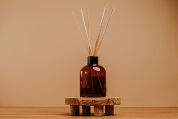Essential oil diffuser with sticks standing on wooden platform. Beige background. Copy space....